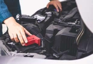 dettaglio di mani che controllano dentro il cofano di un'auto