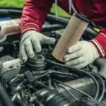 dettaglio di mani di un meccanico con guanti da lavoro che montano un pezzo nel cofano di un'auto