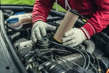 dettaglio di mani di un meccanico con guanti da lavoro che montano un pezzo nel cofano di un'auto